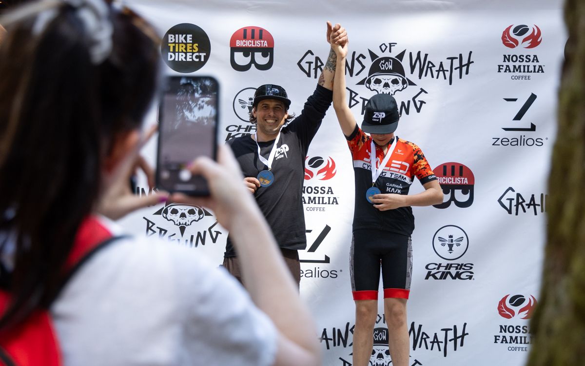 two riders on a podium with nossa familia and bike tires direct logos